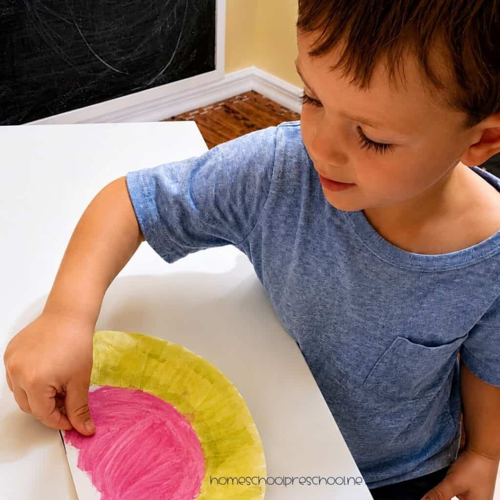 Child adding black watermelon seeds to a painted paper plate craft