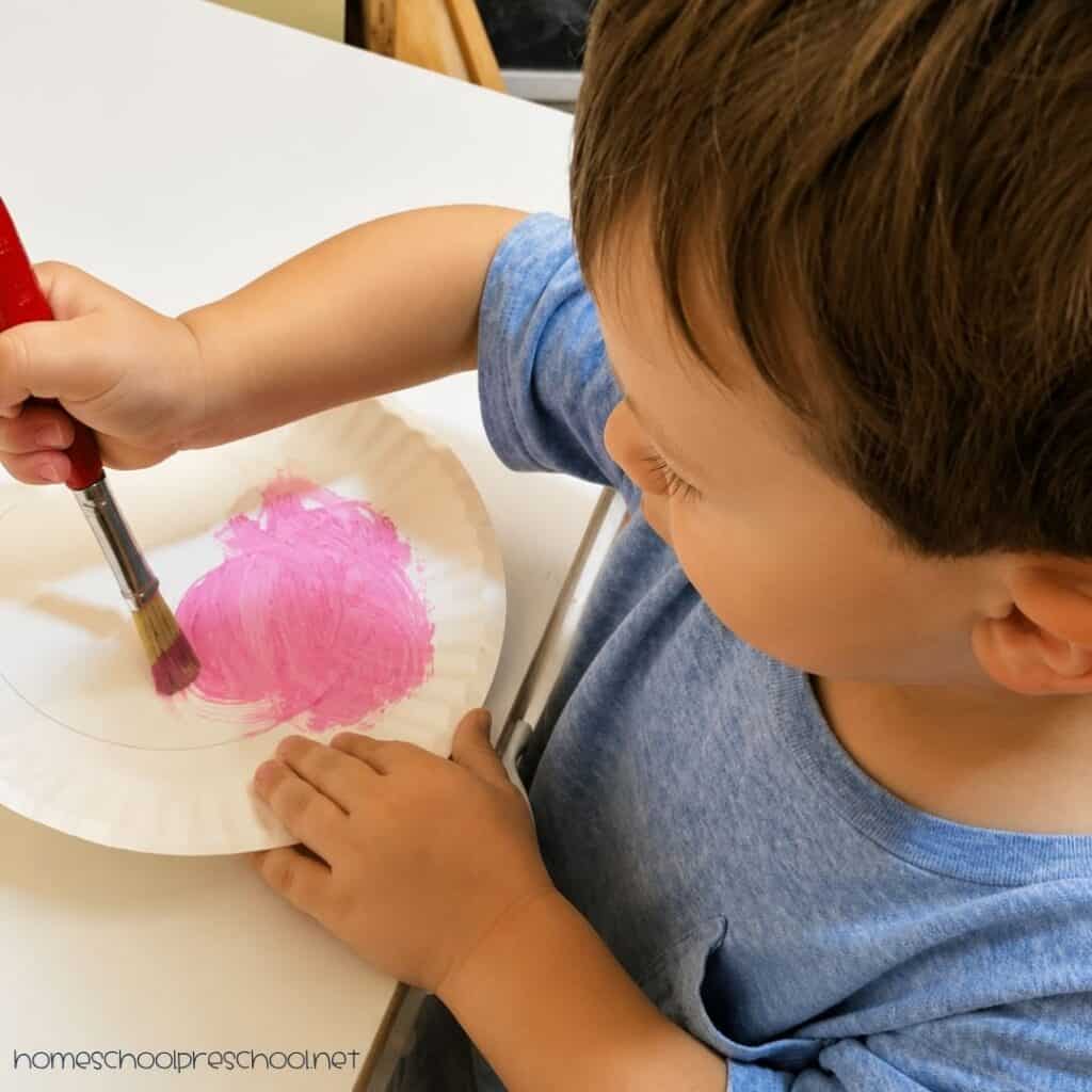 Preschooler painting the center of a paper plate pink for a watermelon craft