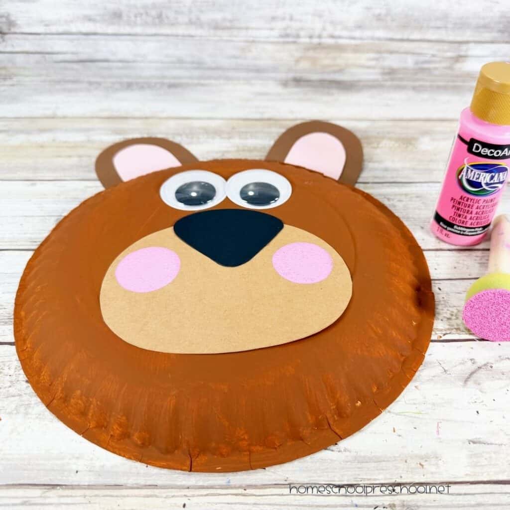 Bear paper plate craft with pink painted cheeks added using a sponge dauber before drawing the bear's smile.