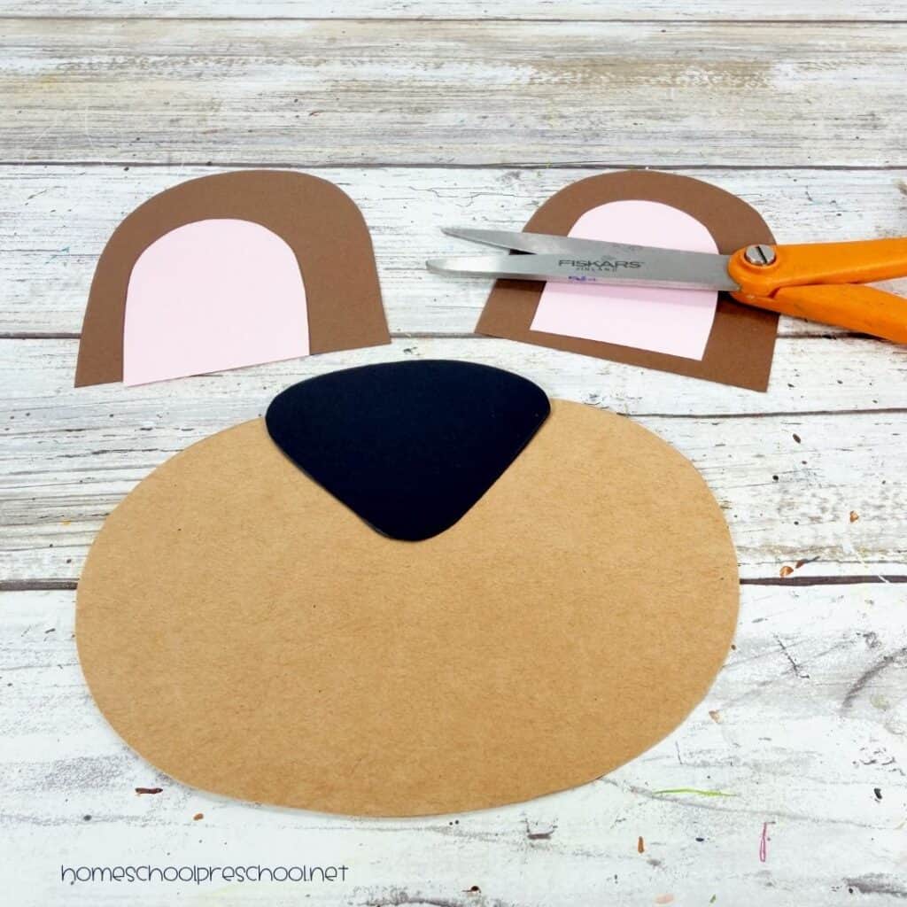 Cut cardstock pieces for a bear paper plate craft, including the ears, muzzle, and nose, ready to assemble.