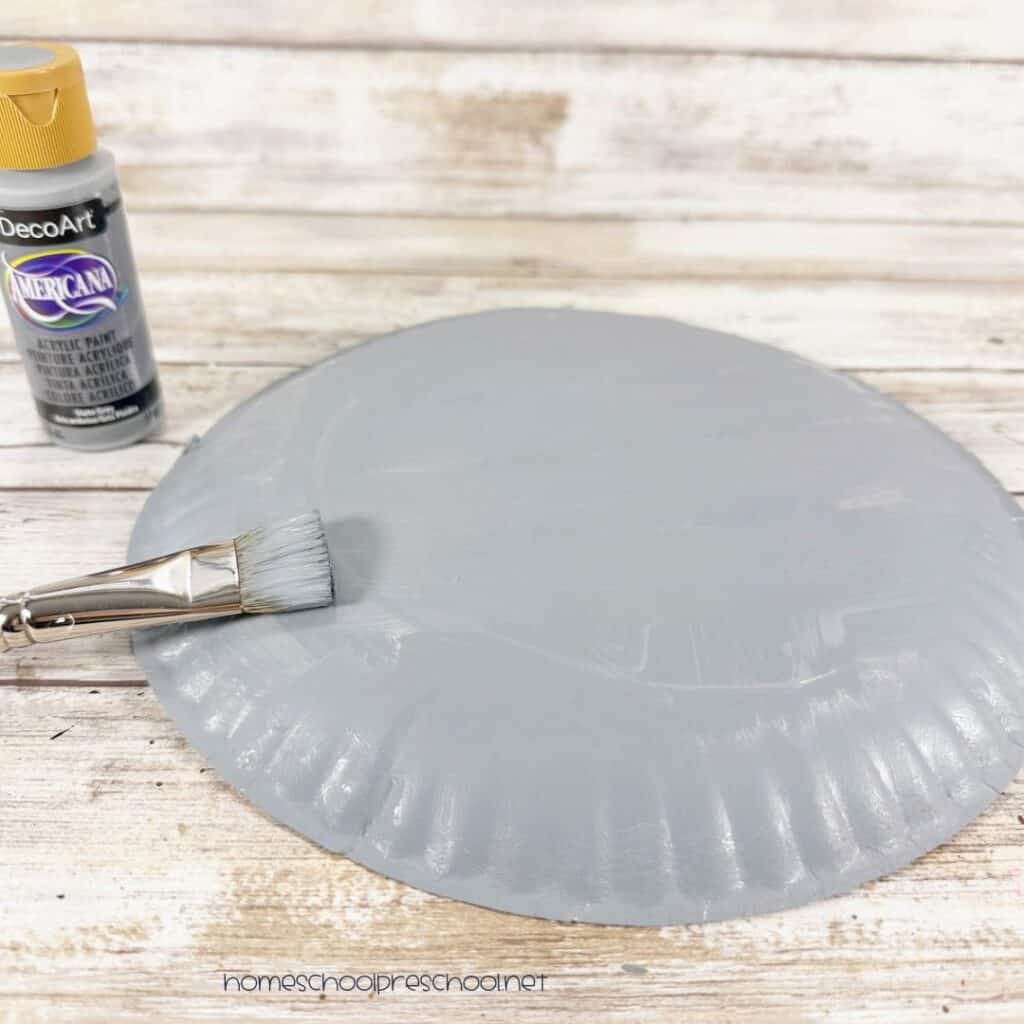 Paper plate being painted gray with a paintbrush for an easy paper plate hippo craft.