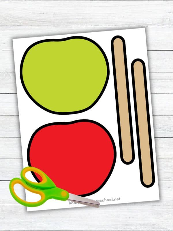 Candy apple craft printable template featuring red and green apple cutouts, two tan sticks, and child-safe scissors for a preschool cut-and-paste activity.
