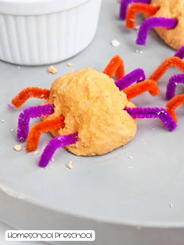 Orange baking soda spider with purple and orange pipe-cleaner legs on a tray, ready for googly eyes.