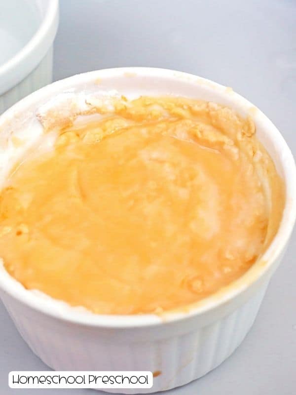 Orange baking soda mixture in a white ramekin for a fizzy spiders Halloween science experiment.