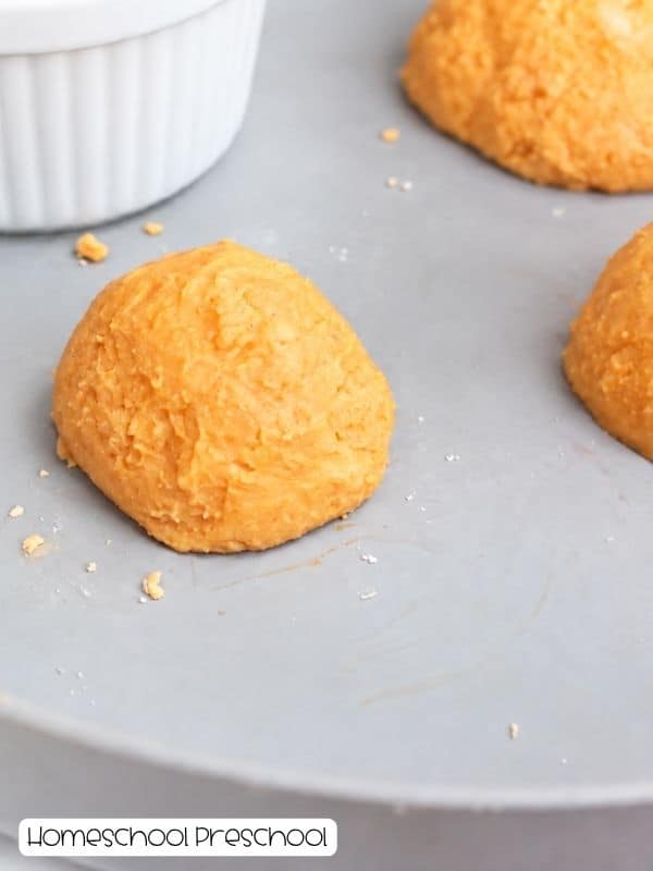 Orange baking soda spider bodies shaped into rounded mounds on a tray for a fizzy spiders experiment.