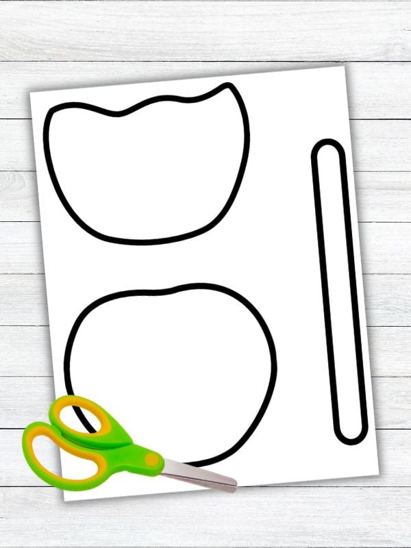 Black-and-white candy apple craft template featuring an apple, candy coating, and stick outlines with child-safe scissors for a preschool cut-and-paste activity.
